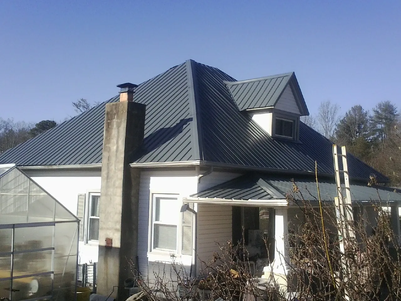 Dark blue standing seam metal roof on a white farmhouse with dormer — Slate & Tile Roof Repair by Roofing Brothers in Hartford