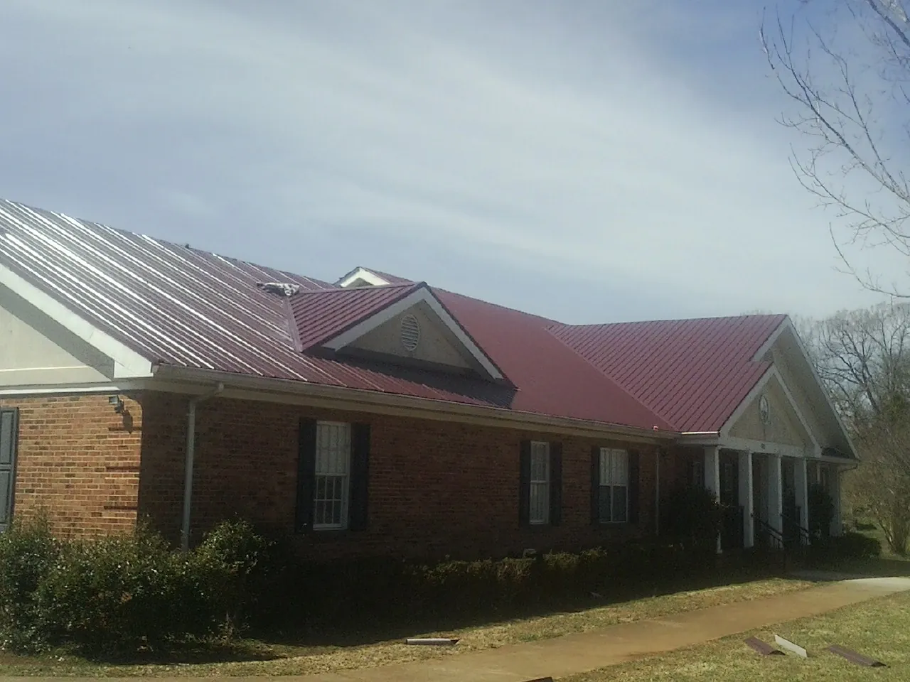 Red metal roof with gabled entries on a long brick building, from a Hail Damage Roof Repair job in Hartford