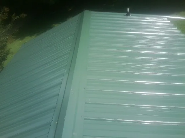 New green metal panels meeting at the ridge of a roof — Flat Roof Repair work by our crew in Hartford