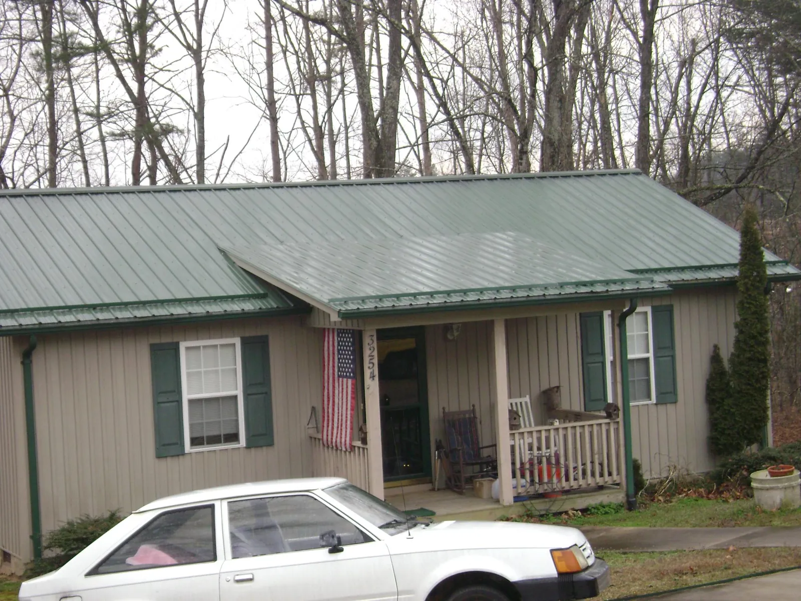 Green metal roof and front porch on a tan sided cottage in Hartford